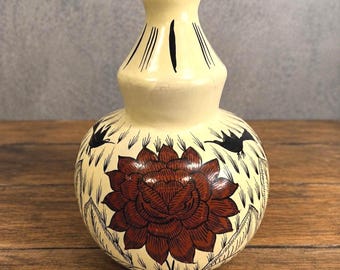 May include: A cream-colored gourd-shaped vase featuring a hand-painted dark red flower at the center. The design includes black line-drawn birds and foliage accents surrounding the flower, with vertical black lines decorating the narrow neck.