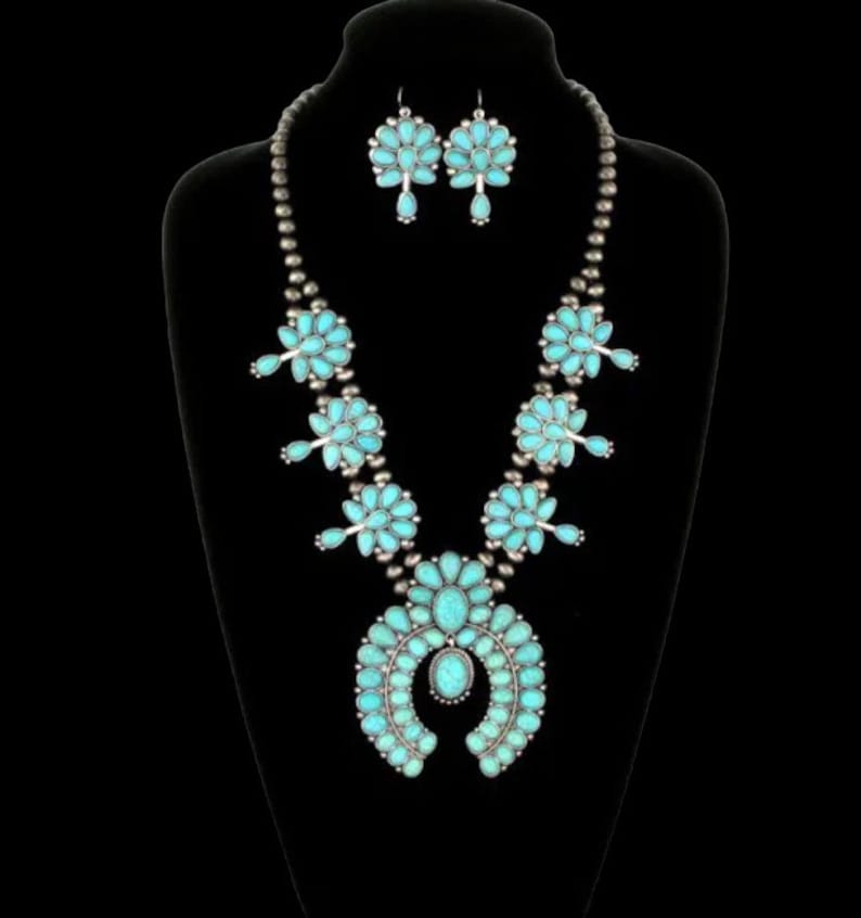 May include: A turquoise and silver Native American style necklace and earrings set. The necklace features a large turquoise horseshoe pendant with smaller turquoise flowers and silver beads. The earrings are also turquoise and silver with a flower design.