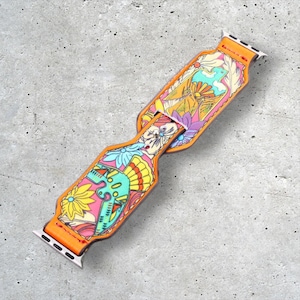 Op de afbeelding: Een kleurrijk, gepatroneerd horlogebandje met oranje leren accenten. Het bandje is ontworpen voor een Apple Watch en heeft een bloemen- en geometrisch ontwerp.