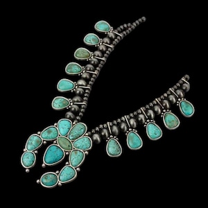 Puede incluir: Un collar de plata con piedras turquesas. El collar presenta un diseño floral central y piedras turquesas en forma de lágrima. El collar tiene un fondo oscuro.