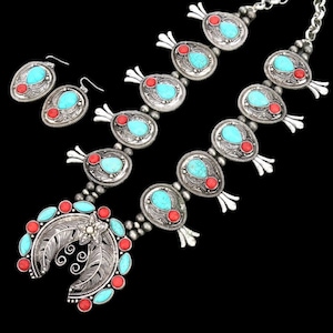 May include: A silver necklace featuring turquoise and coral stones. The necklace has a large, crescent-shaped pendant with a feather design. The necklace also includes a pair of matching earrings.