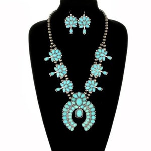 May include: A turquoise and silver necklace and earrings set. The necklace features a large turquoise pendant in the shape of a horseshoe, with smaller turquoise stones surrounding it. The earrings are also turquoise and silver, with a cluster of turquoise stones.