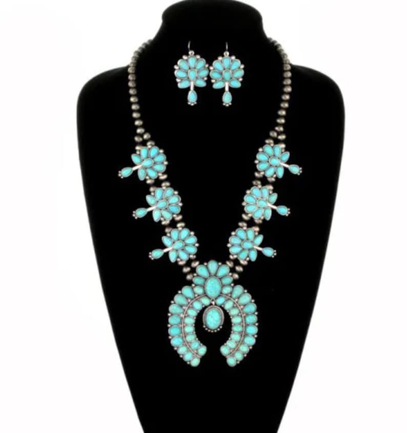 May include: A turquoise and silver necklace and earrings set. The necklace features a large turquoise pendant in the shape of a horseshoe, with smaller turquoise stones surrounding it. The earrings are also turquoise and silver, with a cluster of turquoise stones.