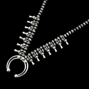 Puede incluir: Un collar de cuentas negras y plateadas con un colgante plateado en forma de herradura. El collar tiene una franja de cuentas plateadas que cuelgan de él.