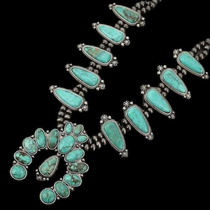 Puede incluir: Un collar de turquesa y plata con un gran colgante de turquesa en forma de herradura. El collar está hecho de pequeñas cuentas de plata y tiene un total de 15 piedras turquesa.