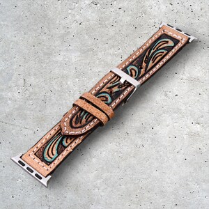 May include: A brown leather Apple Watch band with a turquoise and brown floral design. The band has white stitching and a silver buckle.