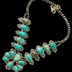 Puede incluir: Un collar de plata con piedras turquesas en forma de lágrima. El collar presenta una cadena de cuentas y un cierre decorativo. Las piedras turquesas están engastadas en engastes de plata ornamentados, creando un contraste llamativo.