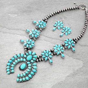 May include: A turquoise and silver necklace and earrings set. The necklace features a large turquoise pendant in the shape of a horseshoe, surrounded by smaller turquoise stones. The earrings are also made of turquoise and silver, and feature a cluster of turquoise stones.