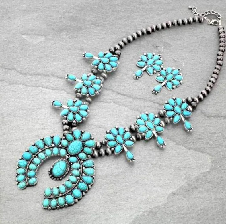 May include: A turquoise and silver necklace and earrings set. The necklace features a large turquoise pendant in the shape of a horseshoe, surrounded by smaller turquoise stones. The earrings are also made of turquoise and silver, and feature a cluster of turquoise stones.