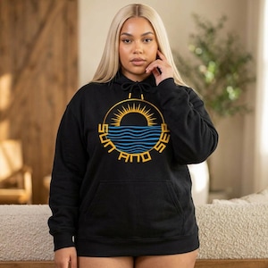 May include: Black hoodie with a front pocket and drawstring hood. The hoodie features a circular graphic with a yellow sun, blue waves, and the words "SUN AND SEA" in yellow block letters. The hoodie is made of a soft material.
