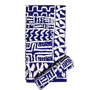 Könnte beinhalten: Ein gefalteter Stoff mit blau-weißem Muster, möglicherweise eine Tischdecke oder ein Textil, mit einem passenden aufgerollten Stück. Das Design zeigt geometrische Formen und Muster in Weiß auf blauem Hintergrund. Der Stoff ist rechteckig.