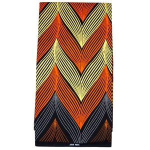 Könnte beinhalten: Rechteckiger Stoff mit einem lebendigen Muster in Orange, Gelb und Schwarz. Das Design zeigt geschwungene Linien, die Blättern oder Federn ähneln, mit einem schwarzen Grund und weißen gepunkteten Akzenten. Der Text "JAVA WAX" ist unten aufgedruckt.