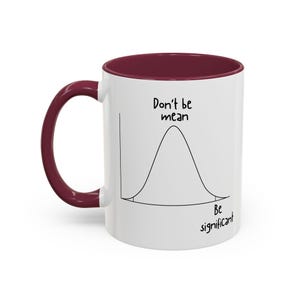 May include: A white ceramic mug with a dark maroon handle and interior rim. The exterior features a black line drawing of a bell curve graph with the text "Don't be mean" above the peak and "Be significant" positioned below the right tail.