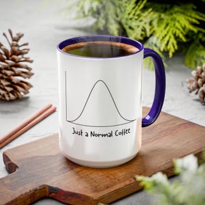 May include: A white ceramic mug with a dark blue interior and handle. The exterior features a black line drawing of a bell curve graph above the text "Just a Normal Coffee" in a simple, handwritten-style font. The mug is filled with dark coffee.