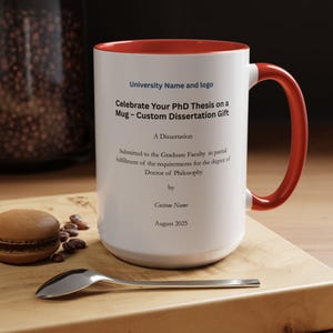 May include: White ceramic mug with a red interior and handle. The mug has text that reads "Celebrate Your PhD Thesis on a Mug - Custom Dissertation Gift" and other details. A spoon and a pastry are on the wooden surface.