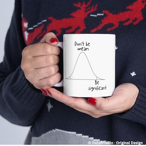 May include: A white ceramic mug featuring a black line drawing of a bell curve distribution graph. The text above the curve reads Don't be mean and the text below the curve reads Be significant. The mug has a simple handle and a smooth finish.
