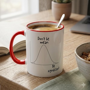May include: A white ceramic mug with a red rim and handle, filled with dark coffee and a silver spoon. The mug features a black line drawing of a bell curve graph with the text "Don't be mean" above the peak and "Be significant" below.