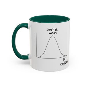 May include: A white ceramic mug with a dark green handle and interior. The exterior features a black line drawing of a bell curve graph with the text "Don't be mean" above the peak and "Be significant" near the tail of the distribution.