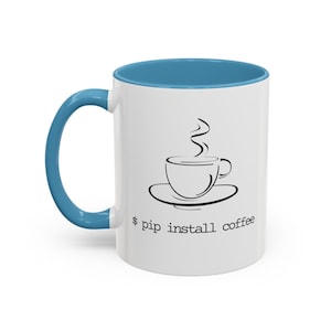 May include: White ceramic mug with a blue rim and handle. The mug features a black and white illustration of a steaming cup of coffee and the text "$ pip install coffee".