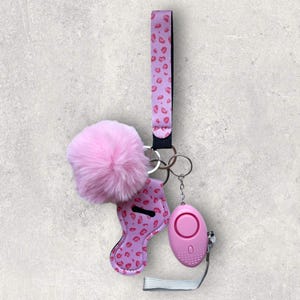 May include: Pink keychain with a fuzzy pom-pom, a pink leopard print hand sanitizer holder, and a pink personal alarm.