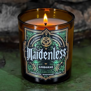 May include: A brown glass candle jar with a gold and green label. The label features the text "Mardenless Ashborne Tarnished" and the words "Make of thyself which ye desire." The candle is surrounded by a green background.