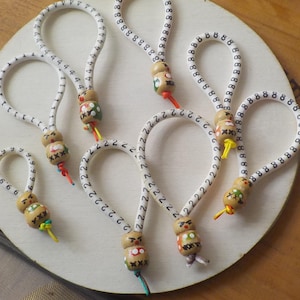 Könnte beinhalten: Eine Sammlung handgefertigter Schlüsselanhänger mit Holzperlen und elastischen Kordeln. Die Perlen sind mit verschiedenen Designs und Farben bemalt, und die Kordeln sind weiß mit schwarzen Zahlen. Jeder Anhänger hat eine Schlaufe.