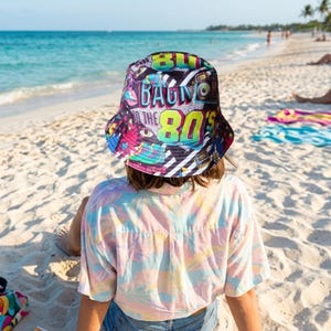 Peut inclure: Un bob noir orné d'un imprimé graphique multicolore vif avec le texte "BACK TO THE 80'S" dans une police dégradée audacieuse. Le motif comprend diverses illustrations sur le thème rétro telles que des cassettes et des motifs géométriques.