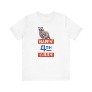 May include: White t-shirt featuring a graphic of two raccoons wearing patriotic bandanas, with the text "HAPPY 4TH OF JULY" in red and blue. The design includes stars and a vintage aesthetic.