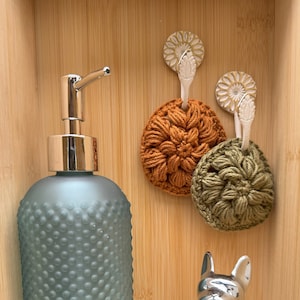 May include: A blue glass soap dispenser with a silver pump, two crocheted scrubbers in orange and green, a silver metal dog figurine, and a crocheted coaster in beige.