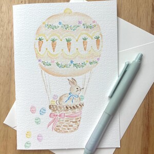 Tarjeta de felicitación con acuarela pintada a mano con un globo aerostático de conejo de Pascua