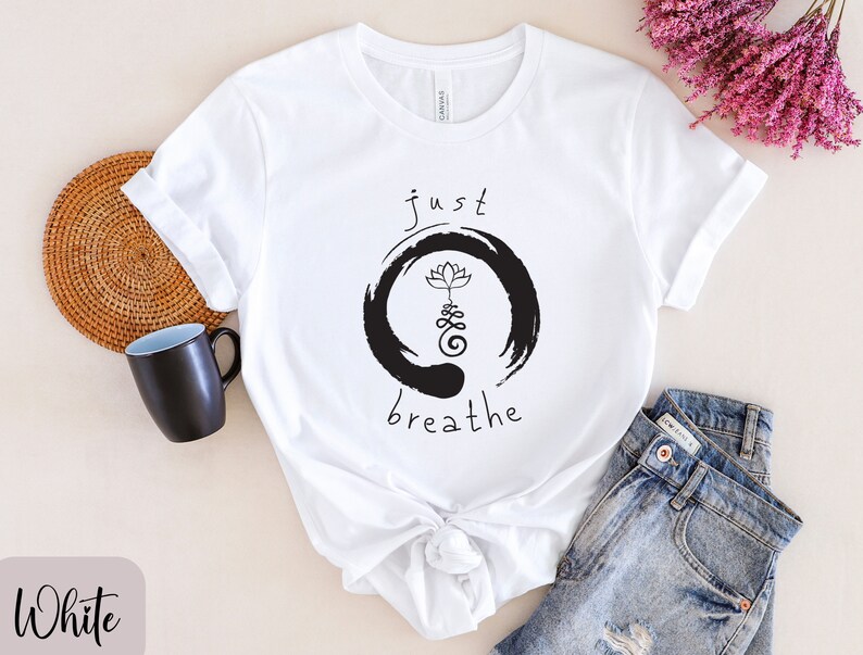 May include: White t-shirt with a black and white graphic design. The graphic features a circle with a lotus flower and the text "just breathe".