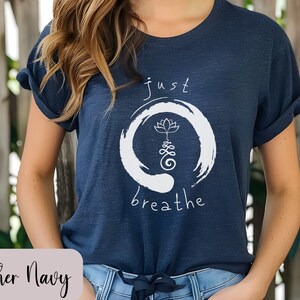 May include: A heather navy blue t-shirt with a white graphic design. The graphic features a circle with a lotus flower and the text "just breathe".