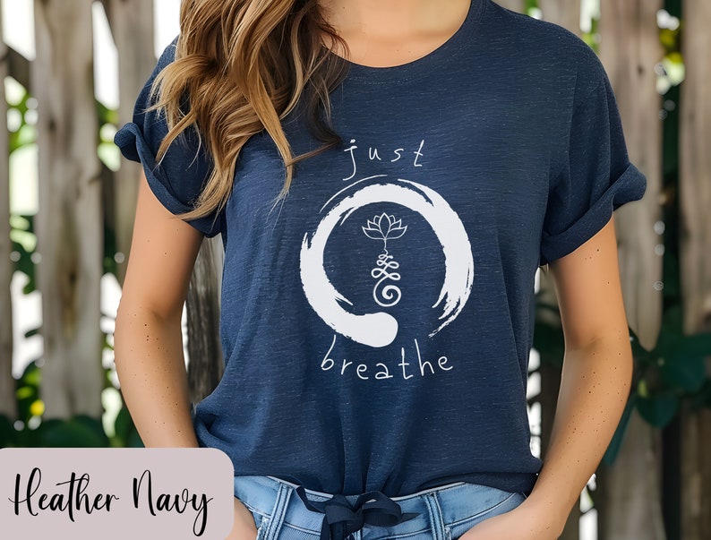 May include: A heather navy blue t-shirt with a white graphic design. The graphic features a circle with a lotus flower and the text "just breathe".