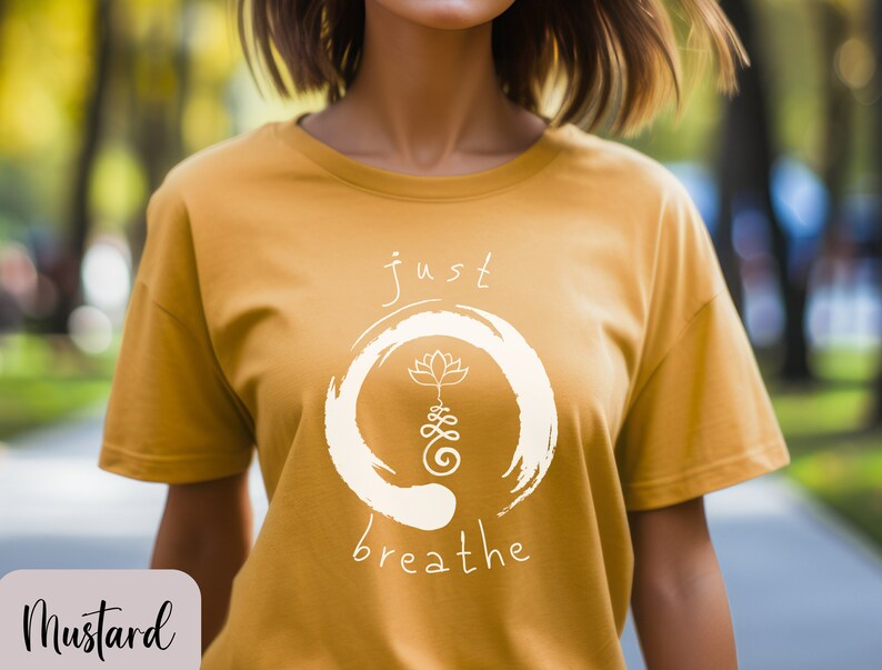 May include: A mustard yellow t-shirt with a white graphic design. The graphic features a circle with a lotus flower and the text "just breathe".