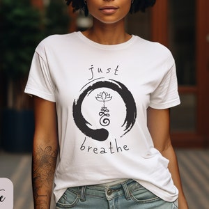 May include: White t-shirt with a black and white graphic design featuring a lotus flower and the text "just breathe".