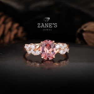 May include: A rose gold engagement ring with a pink oval gemstone surrounded by smaller white gemstones. The ring features a delicate leaf design.