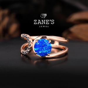 Op de afbeelding: Een ring van roségoud met een blauwe opaal-edelsteen en zwarte diamanten. De ring heeft een uniek ontwerp met een gebogen band en een dubbele band.
