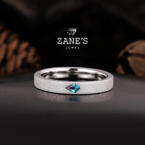 May include: A silver band ring with a textured finish and a small, blue-green gemstone set in the centre.