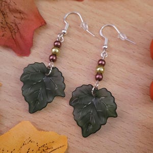 May include: A pair of earrings featuring green leaf charms with silver hooks and brown and green beads.