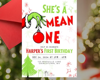 Könnte beinhalten: Eine weiße Weihnachts-Geburtstagseinladung mit einer grünen Grinch-Hand, die einen roten Anhänger hält. Der Text lautet "She's a Mean One" und "Harper's First Birthday" mit Datum und Uhrzeit der Party.