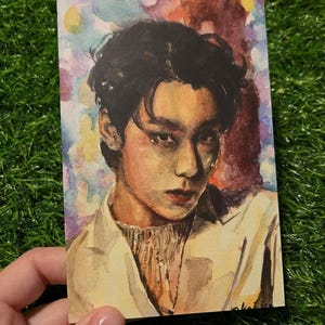 Könnte beinhalten: Aquarellporträt einer Person mit dunklem Haar und einer cremefarbenen Jacke. Das Kunstwerk zeichnet sich durch eine weiche Farbpalette aus, wobei der Fokus auf dem Gesicht und dem Ausdruck des Motivs liegt. Der Hintergrund ist mehrfarbig.