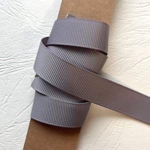 May include: A spool of gray grosgrain ribbon, tightly wound and partially unraveled. The ribbon has a ribbed texture and is displayed against a neutral background. The ribbon is a versatile craft supply.