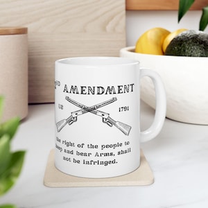 May include: White ceramic mug with the text "2nd Amendment" and "US 1791" and crossed rifles. The mug also includes the phrase "the right of the people to keep and bear Arms, shall not be infringed."