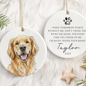 May include: Two white ceramic dog memorial ornaments. One features a watercolour portrait of a golden retriever. The other has a paw print, a poem, the name "Taylor", and the year "2025". Both have gold string for hanging.