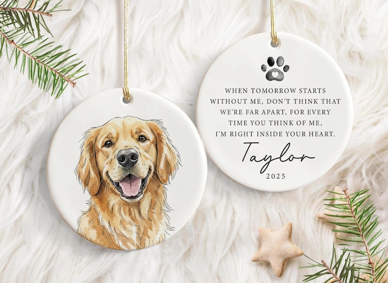 May include: Two white ceramic dog memorial ornaments. One features a watercolour portrait of a golden retriever. The other has a paw print, a poem, the name "Taylor", and the year "2025". Both have gold string for hanging.