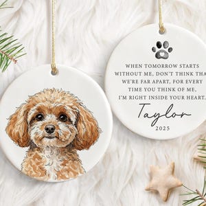 May include: Two white ceramic ornaments with gold hanging strings. One shows a watercolour portrait of a brown dog. The other has a paw print, text, and the name "Taylor" with the year 2025.