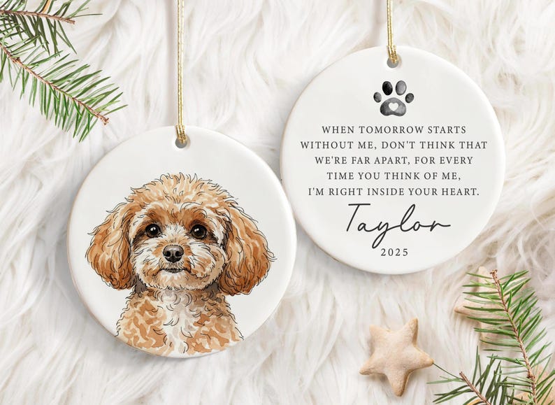 May include: Two white ceramic ornaments with gold hanging strings. One shows a watercolour portrait of a brown dog. The other has a paw print, text, and the name "Taylor" with the year 2025.