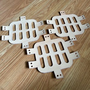 May include: Three unfinished wooden panels with a grid pattern of cut-out ovals and holes around the edges. The panels are arranged in a triangular shape.