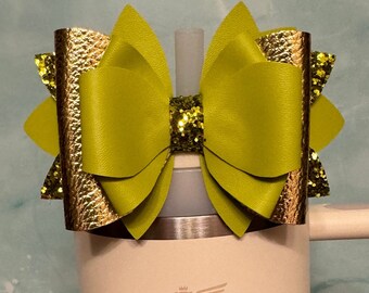 Op de afbeelding: Een limoengroene strik met gouden glitteraccenten is bevestigd aan een witte tumbler met een gouden berenlogo. De strik is gemaakt van imitatieleer en heeft een gelaagd ontwerp.