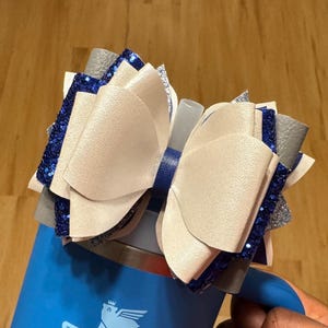 May include: A white and silver bow with blue glitter accents, tied around a blue tumbler.